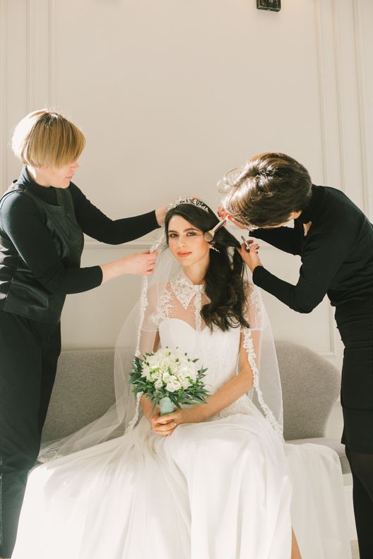 Happy bride in white dress with dressmaker and makeup artist